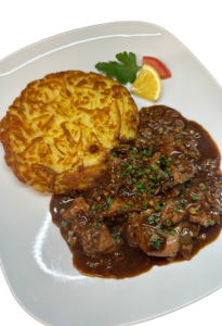 Plate with crispy potato rosti and sliced beef in brown mushroom gravy, garnished with a lemon wedge, tomato slice and parsley leaves. Kalbs Leber mit knusprigen Schweizer Rösti